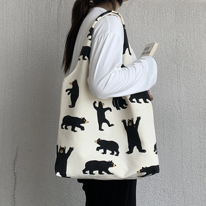 Side view of cream canvas tote bag with black cartoon bear patterns shown on model