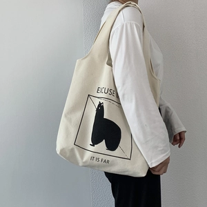 Detailed view of cream canvas tote bag featuring alpaca graphic on a female model