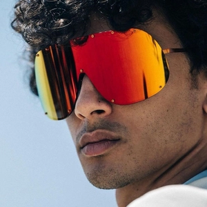 Detail of oversized shield sunglasses with red-orange gradient lenses and gold rivets