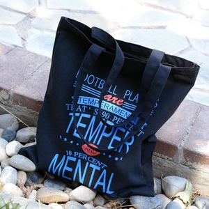 Black canvas tote bag with graphic print and zipper closure on outdoor stone steps