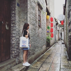 Detail of white canvas tote bag with artistic letter print shown in a street scene