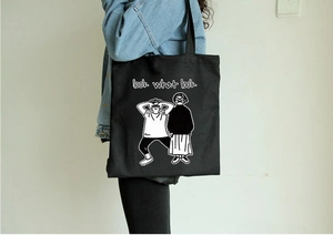 Dettaglio della borsa tote in tela nera con stampa fumetto e slogan sulla spalla