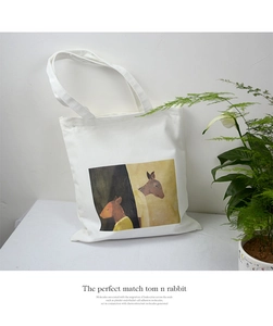 Detail of white canvas tote bag featuring artistic cartoon deer illustration and dual straps