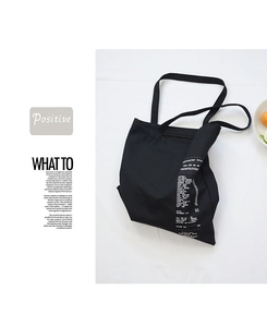 Detail of black canvas tote bag featuring white creative receipt print and long shoulder straps