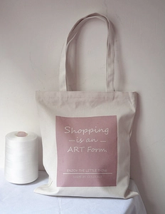 Close-up of canvas tote bag featuring pink square print and artistic typography detail