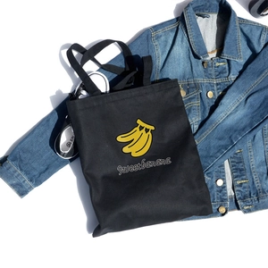 Close-up of black canvas tote bag featuring sweet banana print for daily casual use