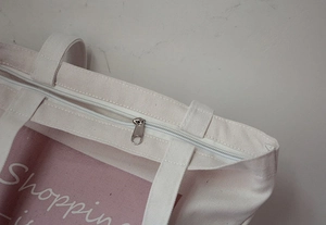 Close-up of metal zipper closure and durable stitching on beige canvas tote bag