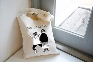 Dettaglio della borsa tote in tela beige con illustrazione nera e testo dello slogan
