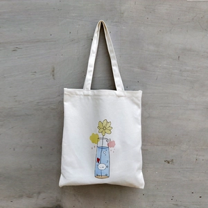 Detail of white canvas tote bag featuring a minimalist sunflower illustration with handles
