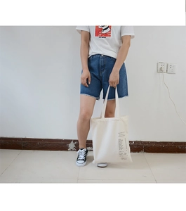 Detail of off-white canvas tote bag with black minimalist typography print and twin handles