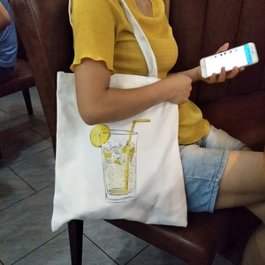 Close-up of a white canvas tote bag with lemon soda illustration in a casual setting