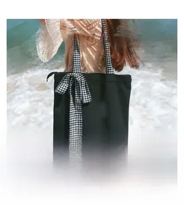 Detail of black canvas tote bag with checkered bow strap on a seaside beach background