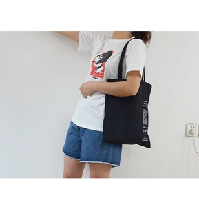 Detail view of a black canvas tote bag showing side white minimalist letter printing