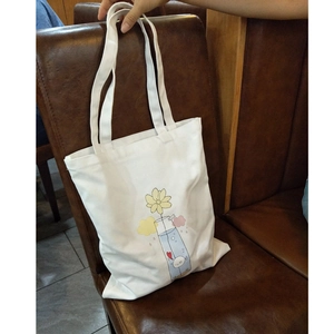 Close-up of white canvas tote bag with yellow flower illustration on leather background