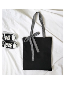 Close-up of black canvas tote bag featuring a checkered bow and matching wide shoulder strap