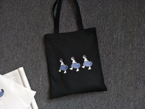 Detail of black canvas tote bag with cartoon girls print on a textured background