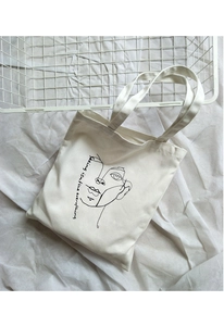 Flat lay of cream canvas tote bag with artistic face print and minimalist text design
