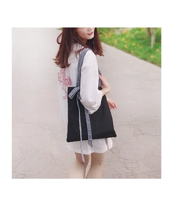 Detail of black canvas tote bag featuring a decorative gingham bow on the shoulder strap