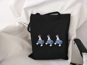 Detail of black canvas tote bag with trio of walking girls illustration and shoulder straps