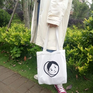 Detail of white canvas tote bag with black cartoon illustration worn with a trench coat