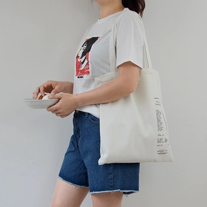 Minimalist white canvas tote bag with black shopping list print shown on a female model