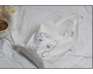 Détail du dessin abstrait de visage sur un sac cabas en toile blanche minimaliste