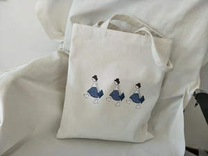 Detailed view of beige canvas tote bag with blue floral dress girl illustration print