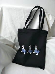 Detail shot of black canvas tote bag featuring three cute cartoon girl illustrations