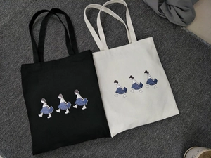 Flat lay detail of black and beige canvas tote bags with girl cartoon prints