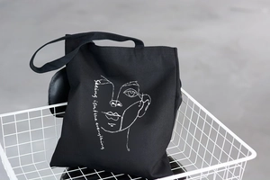 Detail of minimalist black canvas tote bag featuring white line art and artistic text