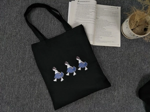 Close-up of black canvas tote bag featuring cute cartoon girl prints and sturdy handles