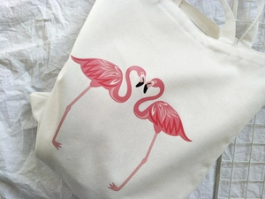 Detailed view of white canvas tote bag featuring two pink flamingo illustrations
