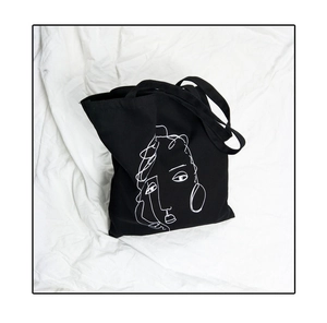 Détail de l'imprimé visage minimaliste blanc sur un grand sac cabas en toile noire
