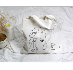Détail du sac en toile blanche avec portrait abstrait en lignes noires et texture épaisse