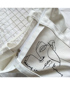 Detail of canvas shoulder bag showing abstract portrait print and metal zipper closure
