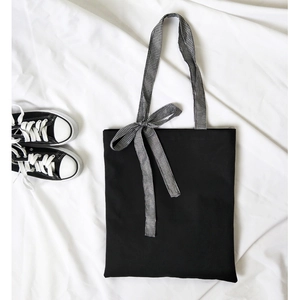 Minimalist black canvas tote bag with gingham ribbon bow detail and top zipper closure