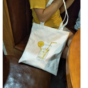 White canvas tote bag with lemon illustration worn by a model in a casual setting