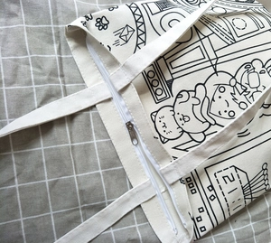 Detail of canvas tote bag featuring black cartoon line art and secure zipper closure