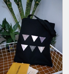 Detail of a black canvas tote bag featuring geometric inverted triangles and wide shoulder strap