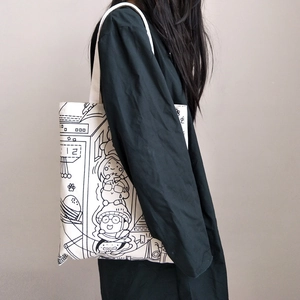 Detail of canvas shoulder bag featuring black manga style illustrations on cream fabric