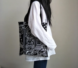 Detail of canvas tote bag with black and white cartoon characters and wide strap