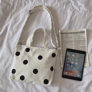 Detailed view of white canvas tote bag with black polka dots featuring iPad for scale