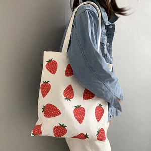 Detail shot of a large white canvas tote bag with vibrant red strawberry prints on shoulder