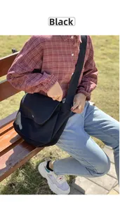 Close-up of black canvas crossbody bag with silver buckle worn in an outdoor park setting