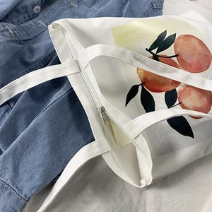Detail view of the silver zipper closure and orange fruit print on white canvas tote bag