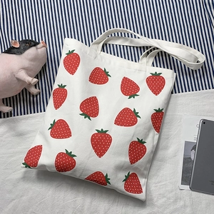 Detail of white canvas tote bag featuring repetitive red strawberry prints and shoulder straps