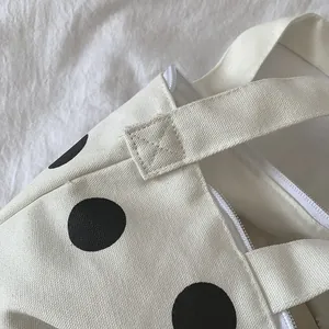 Close-up of reinforced cross-stitch seams and zipper closure on polka dot canvas bag