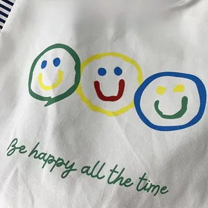 Detail of canvas tote bag featuring colorful smiley face prints and slogan