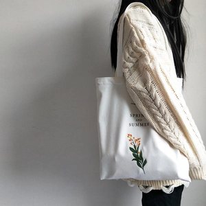 Detailed view of a white canvas tote bag with orange flower print on a person