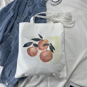 Flat lay of a white canvas tote bag with orange fruit print and blue denim jacket